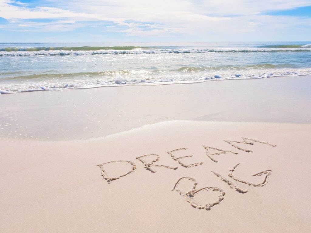 An ocean beach where someone has written "dream big" in the sand. To inspire saving money to make that dream trip a reality.