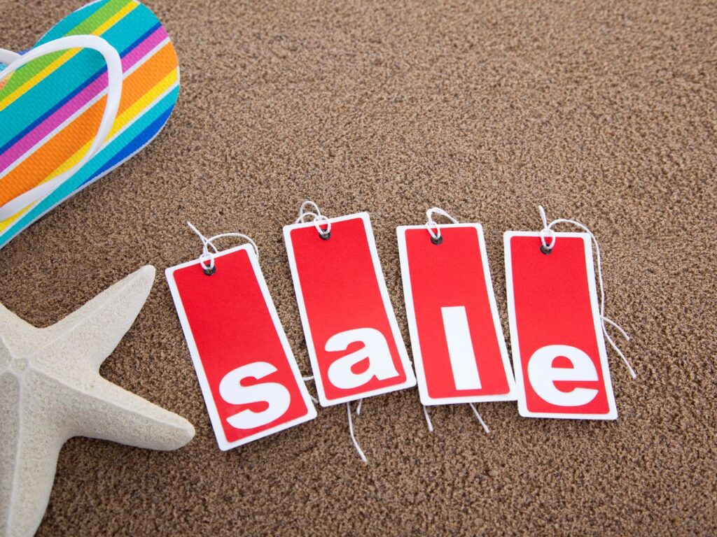 Wait for sales to book your dream trip at a cheaper price. A flip flop, starfish and sales tag on a beach.