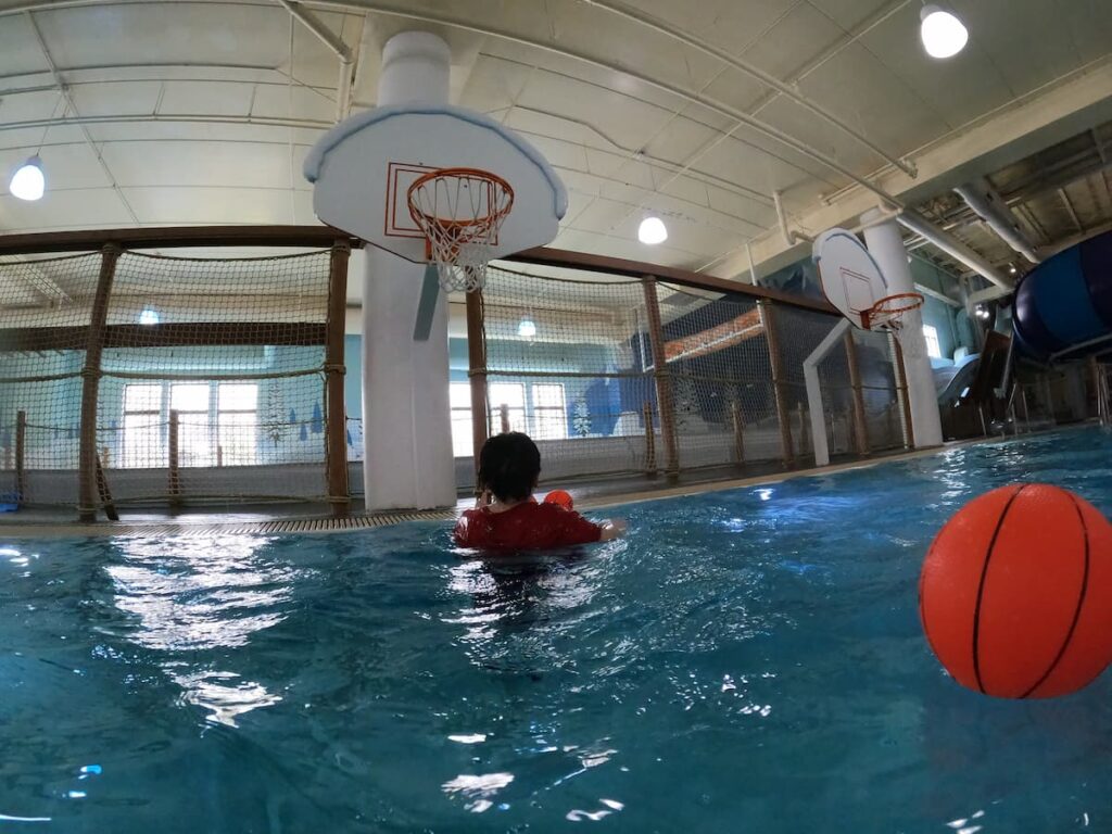 Kids and families playing in Blizzard Bay Activity Pool at Avalanche Bay Indoor Waterpark — a fun pool area with basketball hoops, open swim space, and interactive water features.