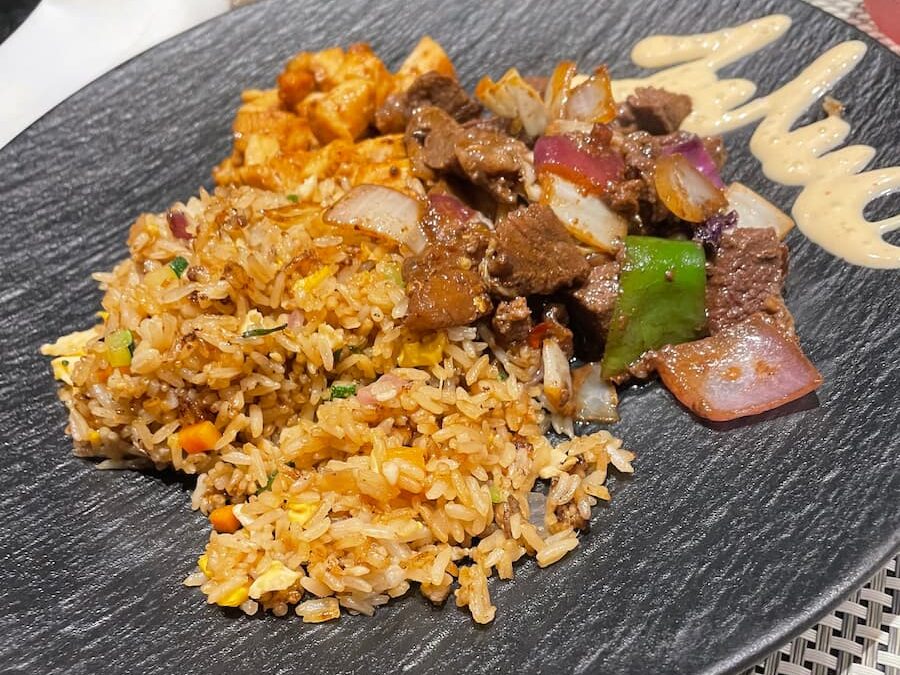 Stir-fried rice dish at Himitsu featuring vegetables and grilled chicken, garnished with green onions and sesame seeds.