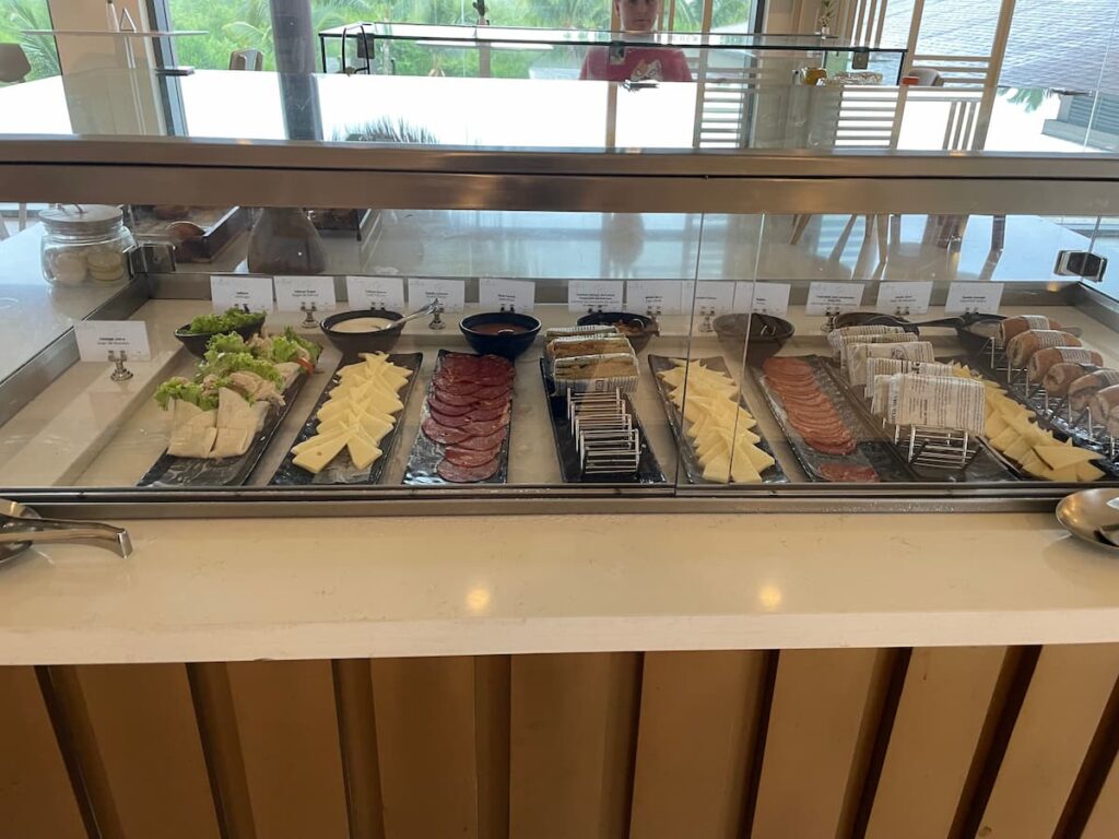 Assorted finger foods at the Preferred Club Lounge, including mini sandwiches, fresh fruit, and pastries on a buffet table.