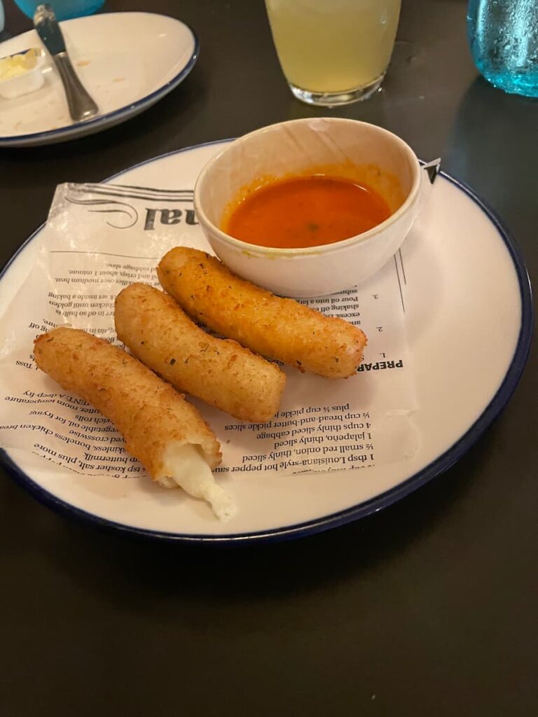 Crispy golden mozzarella sticks served with marinara dipping sauce on a white plate.
