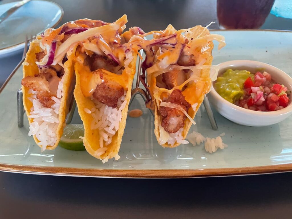 Fresh fish tacos topped with shredded cabbage, salsa, and creamy sauce, served with lime wedges.