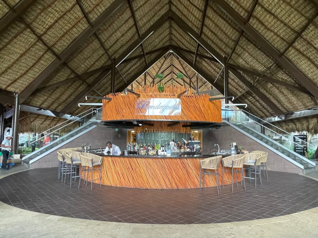 Outdoor Rendezvous Bar at Dreams Flora with thatched roof, bar stools, and tropical palm trees in the background