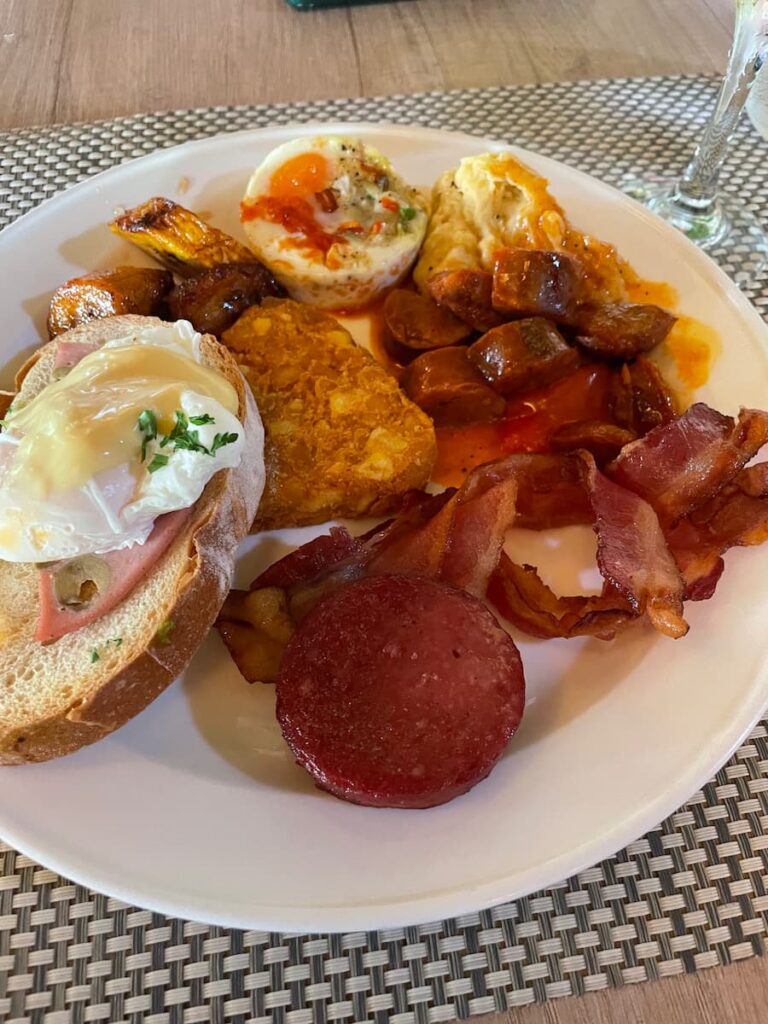Plate of breakfast food at World Café featuring scrambled eggs, fresh fruit, toast, and bacon at Dreams Flora Resort.