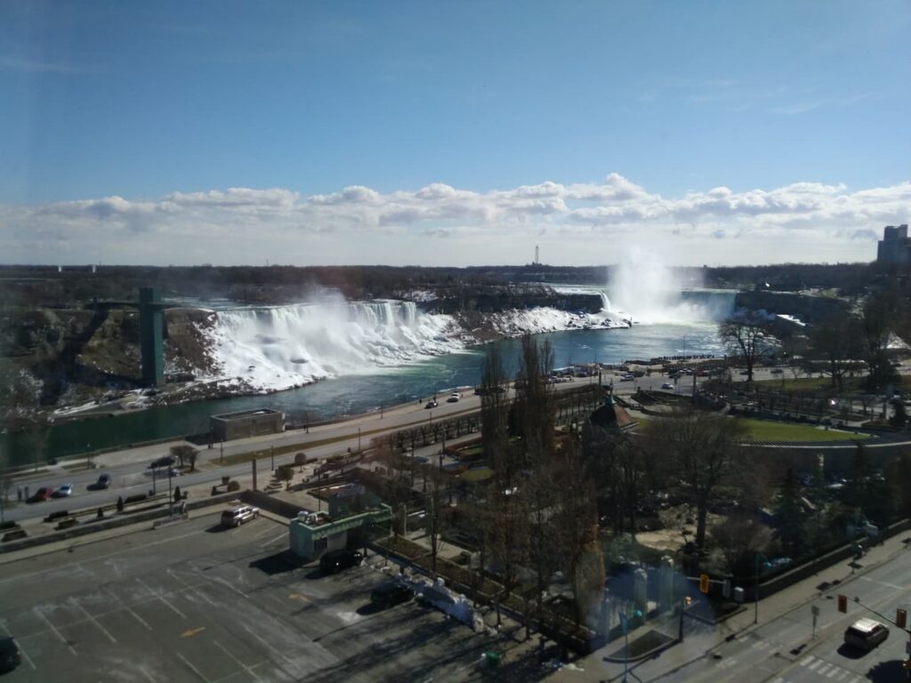 View of Niagara Falls from hotel window with a panoramic perspective of the cascading waterfalls and mist rising above the river.